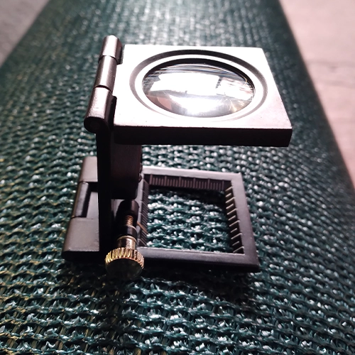 لنز بزرگ‌نما روی ماده توری سایبان، نمایش‌دهنده بافت ریز و ساختار فشرده که تضمین‌کننده کیفیت برتر برای استفاده‌های کشاورزی و ساختمانی است